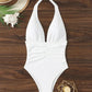 White halter one-piece swimsuit with ruched waist, beach hat, seashell, and gold decor on wood