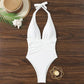 White halter neck one-piece swimsuit with ruched waist, beach hat, palm leaf, and seashell on wood
