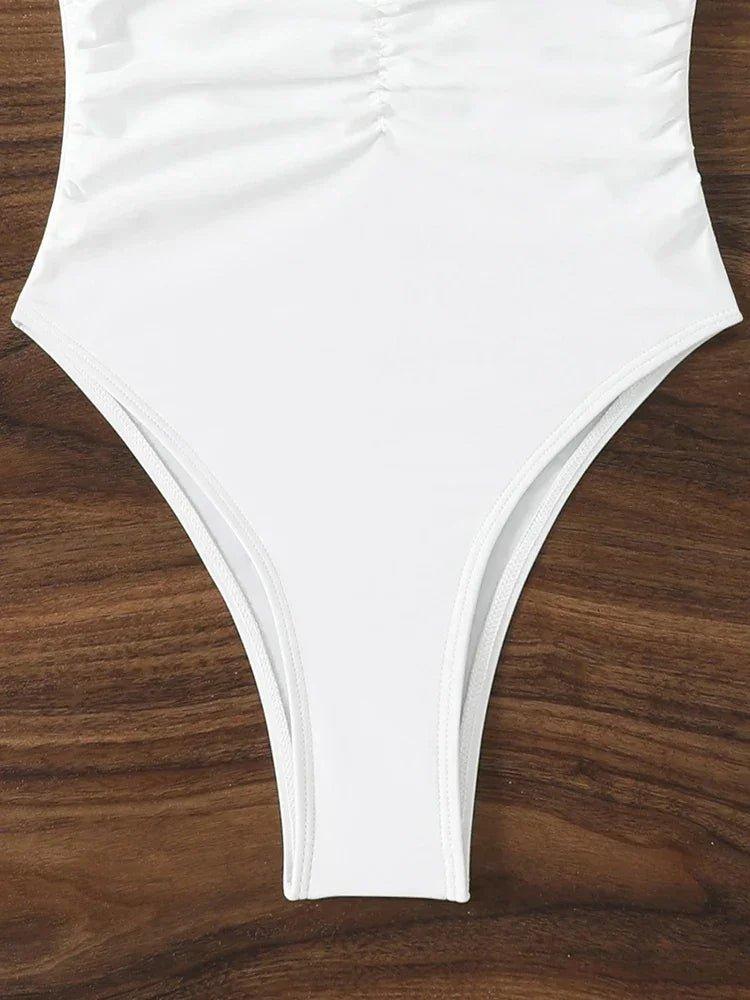 White one-piece swimsuit with ruched front, high-cut legs, laid on wood surface