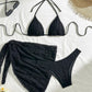 Black textured bikini set with tie-front top, matching bottoms, and sarong, styled with sunglasses and straw hat for beach fashion.