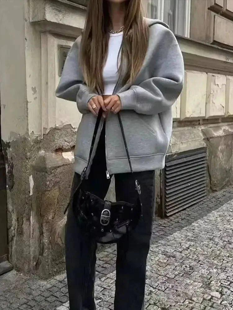 Woman in gray hoodie, black jeans, and studded bag for casual streetwear fashion