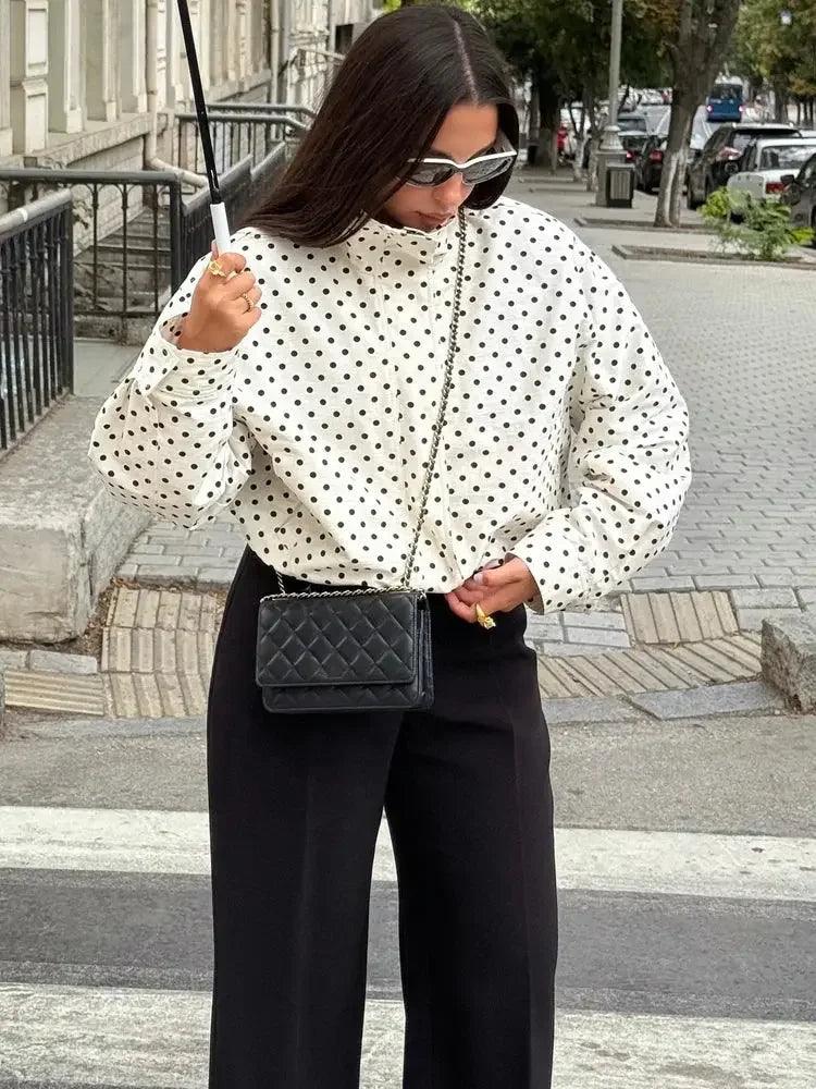 Woman in white polka dot blouse, black pants, and quilted crossbody bag on city street