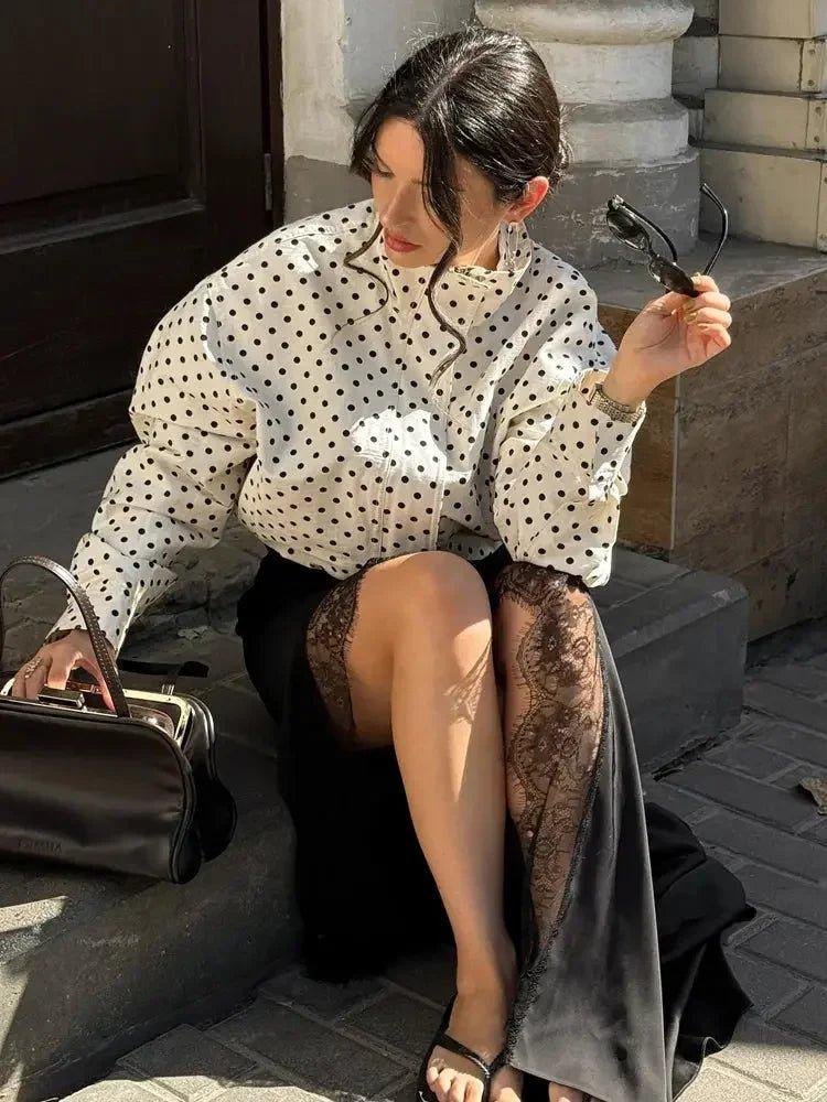 Woman in polka dot blouse and lace skirt, holding sunglasses, stylish street fashion