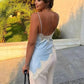 Woman in light blue lace-trimmed backless top and white pants, holding black bag outdoors