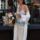 Woman in lace camisole and white robe holding coffee, pink roses nearby, street fashion style