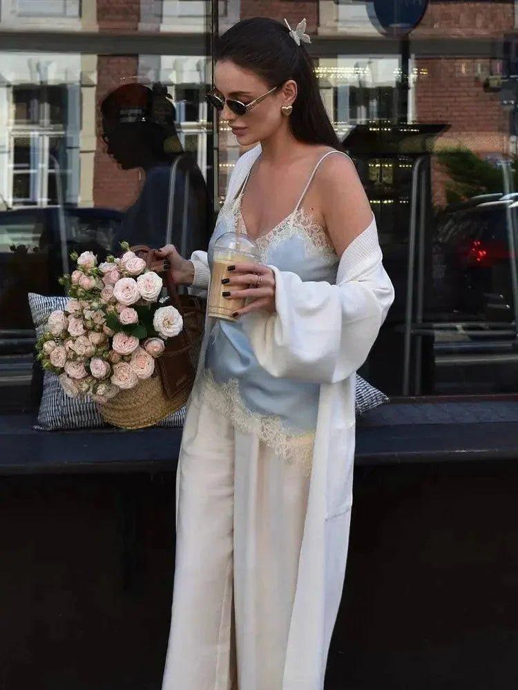 Woman in lace camisole and white robe holding coffee, pink roses nearby, street fashion style