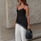 Woman in black lace camisole top and white wide-leg pants, holding black handbag, street style fashion