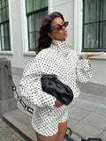 Woman in white polka dot outfit with black clutch and sunglasses, street fashion style