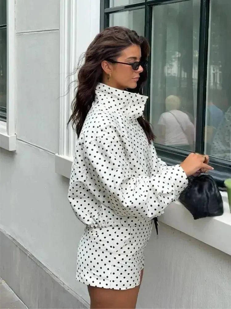 Woman in white polka dot fashion set with high collar, sunglasses, and black clutch, stylish streetwear look