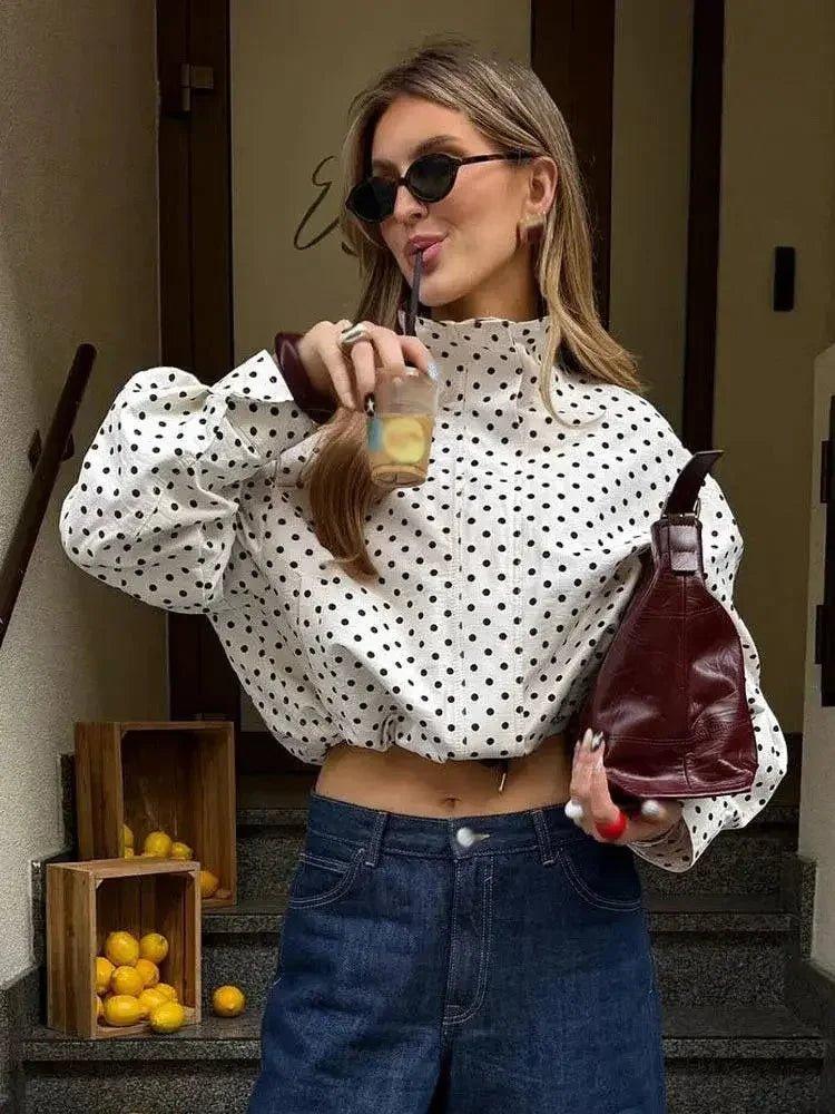 Woman in polka dot crop top and jeans sipping drink, holding burgundy bag, stylish summer fashion
