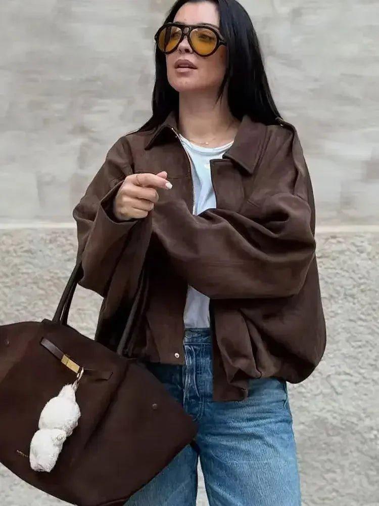 Woman in brown oversized jacket, blue jeans, and yellow sunglasses carrying matching tote bag