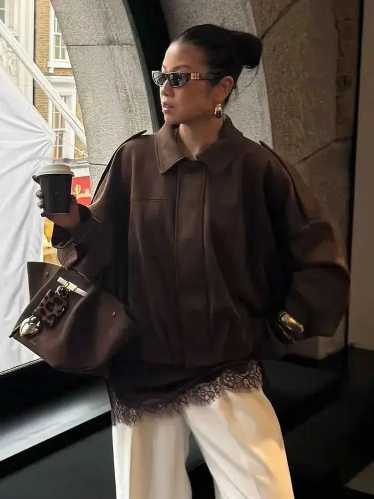 Woman in chic brown jacket, white lace-trim pants, holding coffee, stylish streetwear fashion