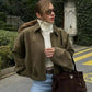 Woman in olive suede jacket, white turtleneck, and jeans with brown handbag, stylish street fashion