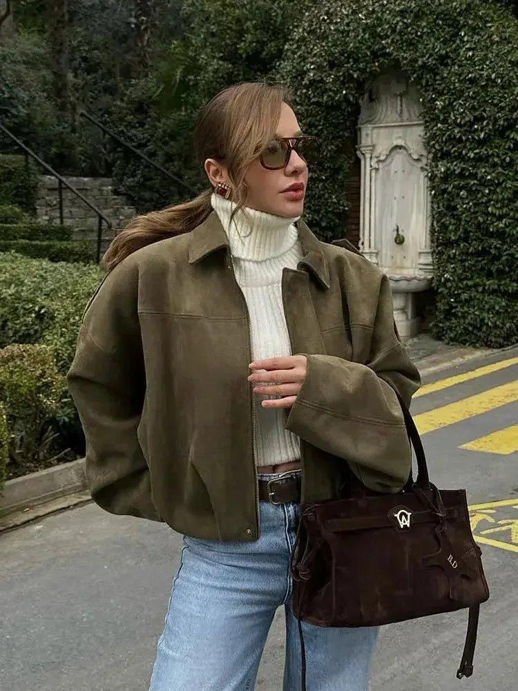 Woman in olive suede jacket, white turtleneck, and jeans with brown handbag, stylish street fashion