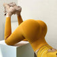 Woman in mustard yellow fitness leggings and matching top, posing on white block with beige sneakers