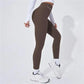 Women's high-waist brown leggings with white text, paired with white long sleeve top and sneakers