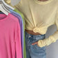 Woman modeling knotted yellow long sleeve top with colorful t-shirts on hangers, casual fashion outfit