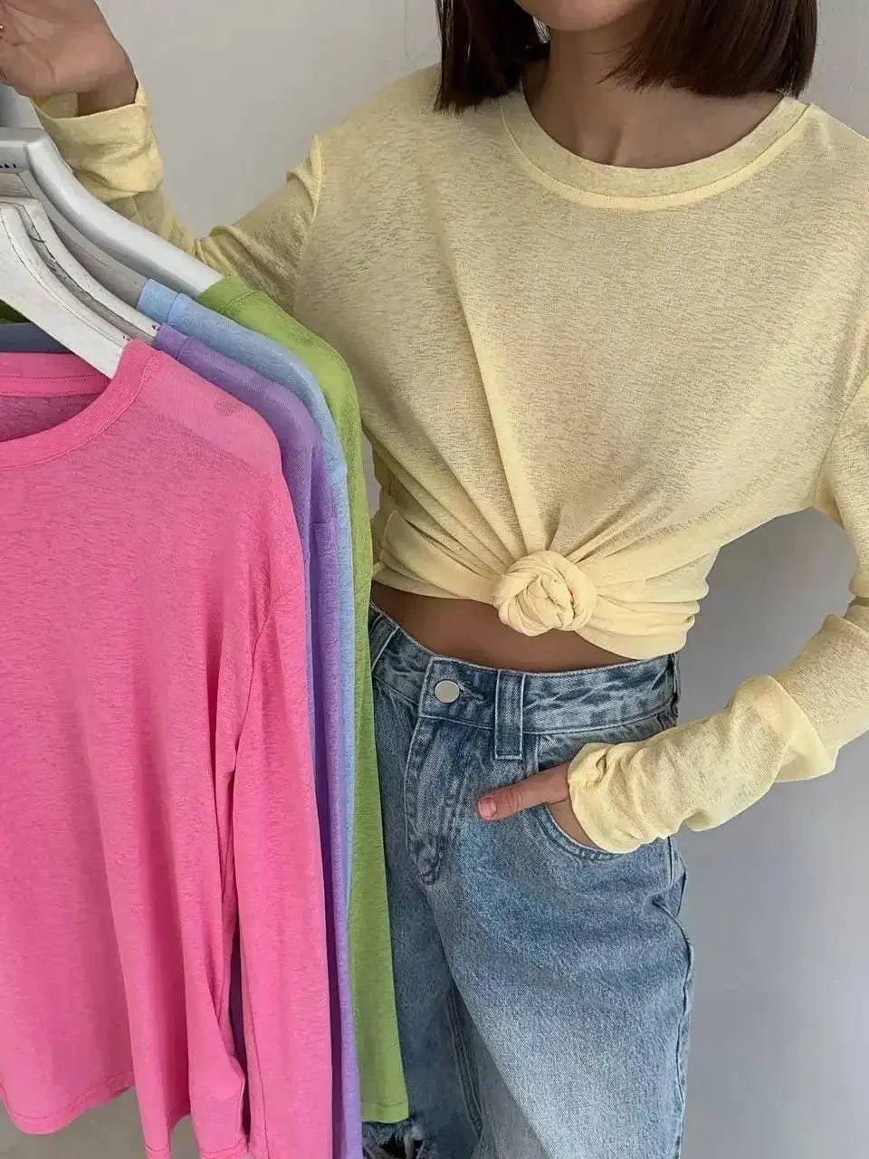 Woman modeling knotted yellow long sleeve top with colorful t-shirts on hangers, casual fashion outfit