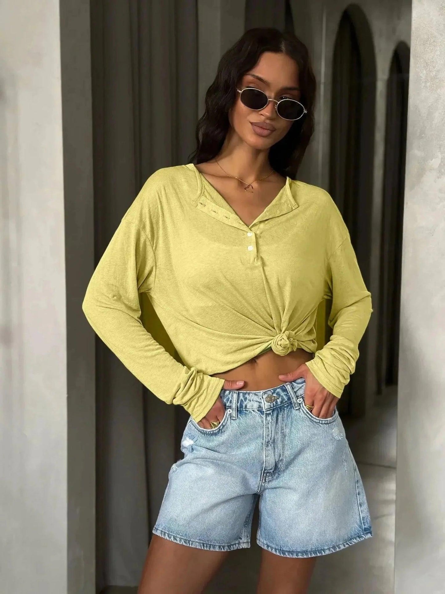 Woman in yellow knotted long sleeve top and denim shorts, stylish summer fashion outfit