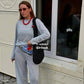Woman in gray loungewear set with red beaded necklace and black woven bag, stylish street fashion