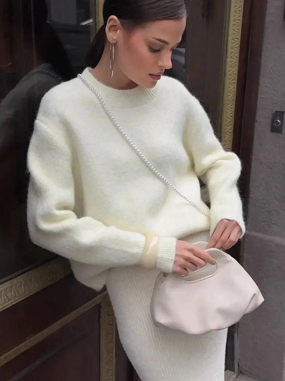 Woman in cozy cream sweater and ribbed skirt, carrying pearl-chain bag, chic street style