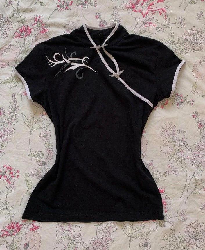 Black women's fashion top with white trim and floral design, laid on floral bedding