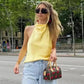 Woman in yellow halter top and jeans, carrying floral handbag, stylish street fashion look