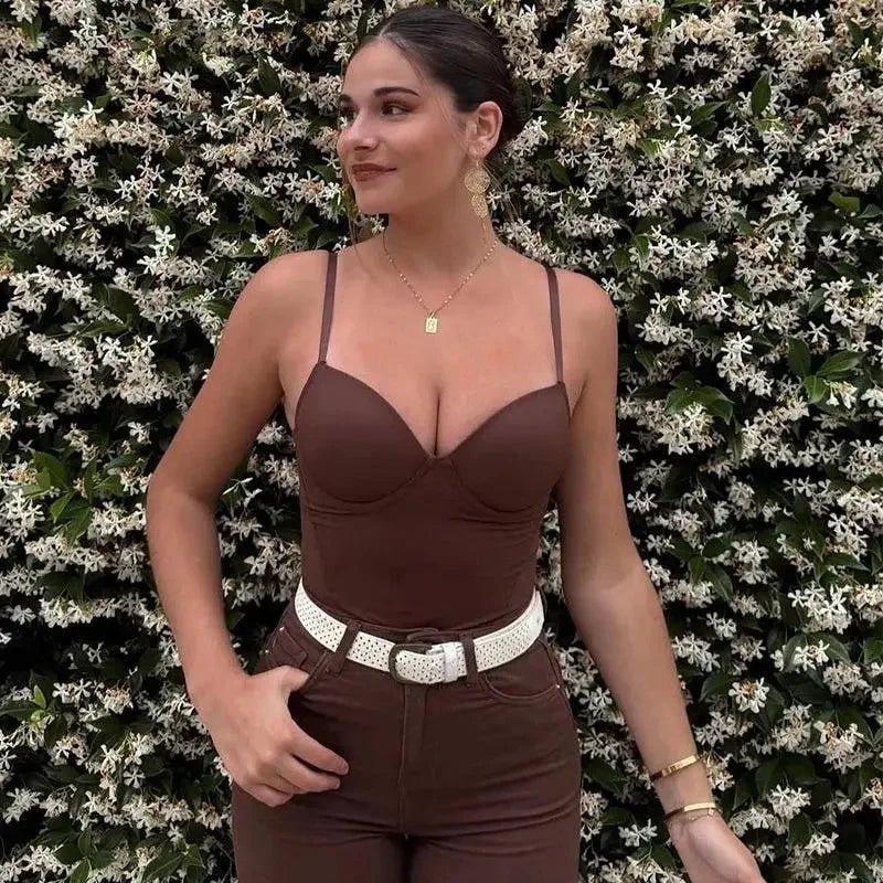 Woman in brown bodysuit with white belt, standing before floral wall — women's fashion outfit