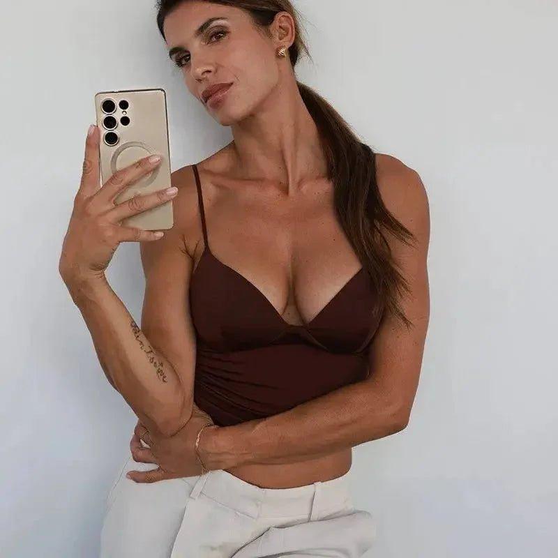 Woman taking selfie in brown strappy top and white pants, showcasing casual fashion style