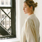 Woman in cream oversized shirt with striped sleeves, standing by window, minimalist fashion style