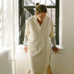 Woman in cream linen dress with striped sleeves, standing by window, casual fashion