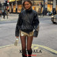 Woman in black leather jacket and gold sequin skirt walking city street, stylish fashion outfit