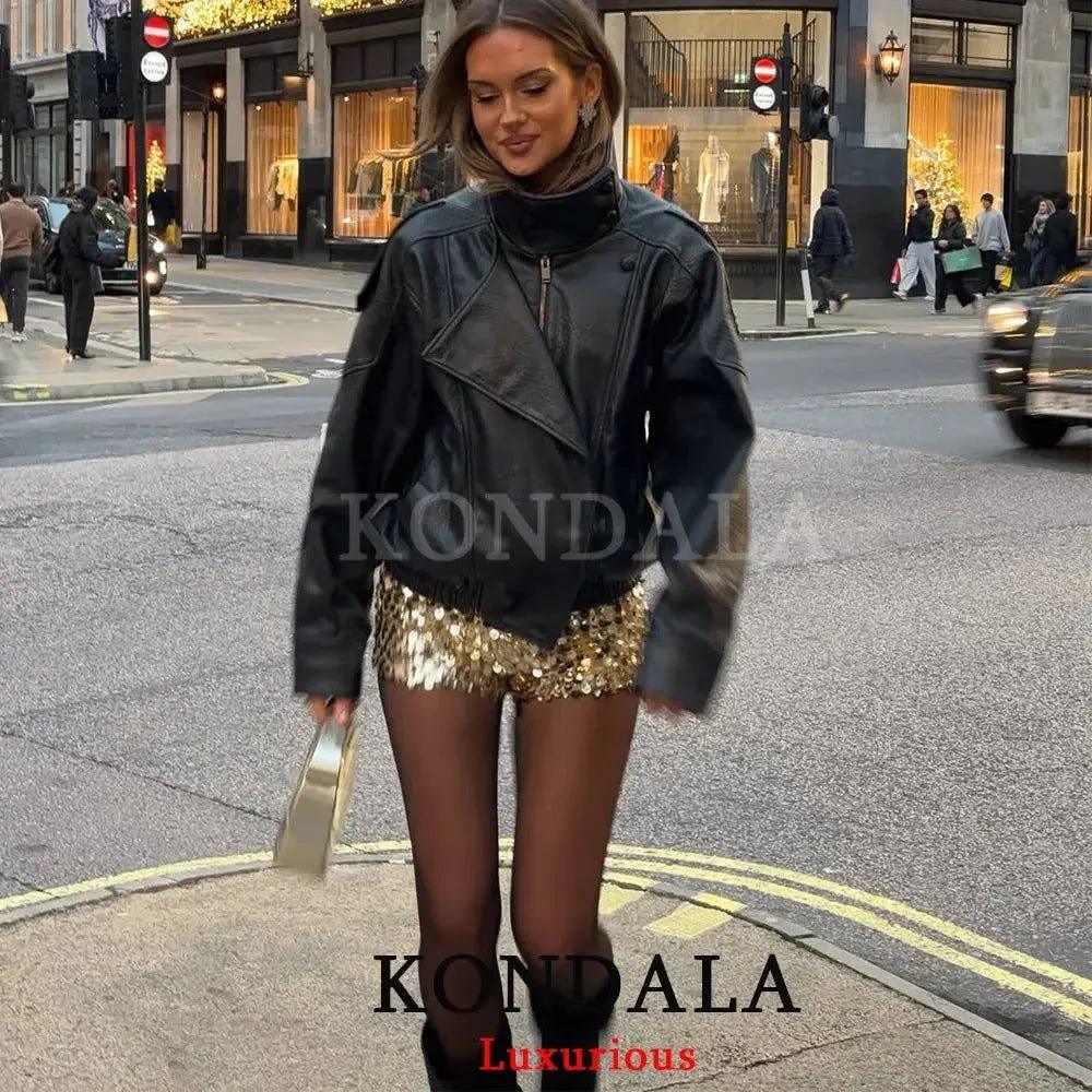 Woman in black leather jacket and gold sequin skirt walking city street, stylish fashion outfit
