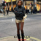 Woman in black leather jacket, gold sequin shorts, and boots on city street, stylish fashion outfit