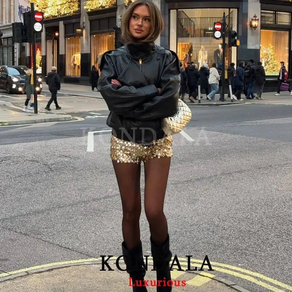 Woman in black leather jacket, gold sequin shorts, and boots on city street, stylish fashion outfit
