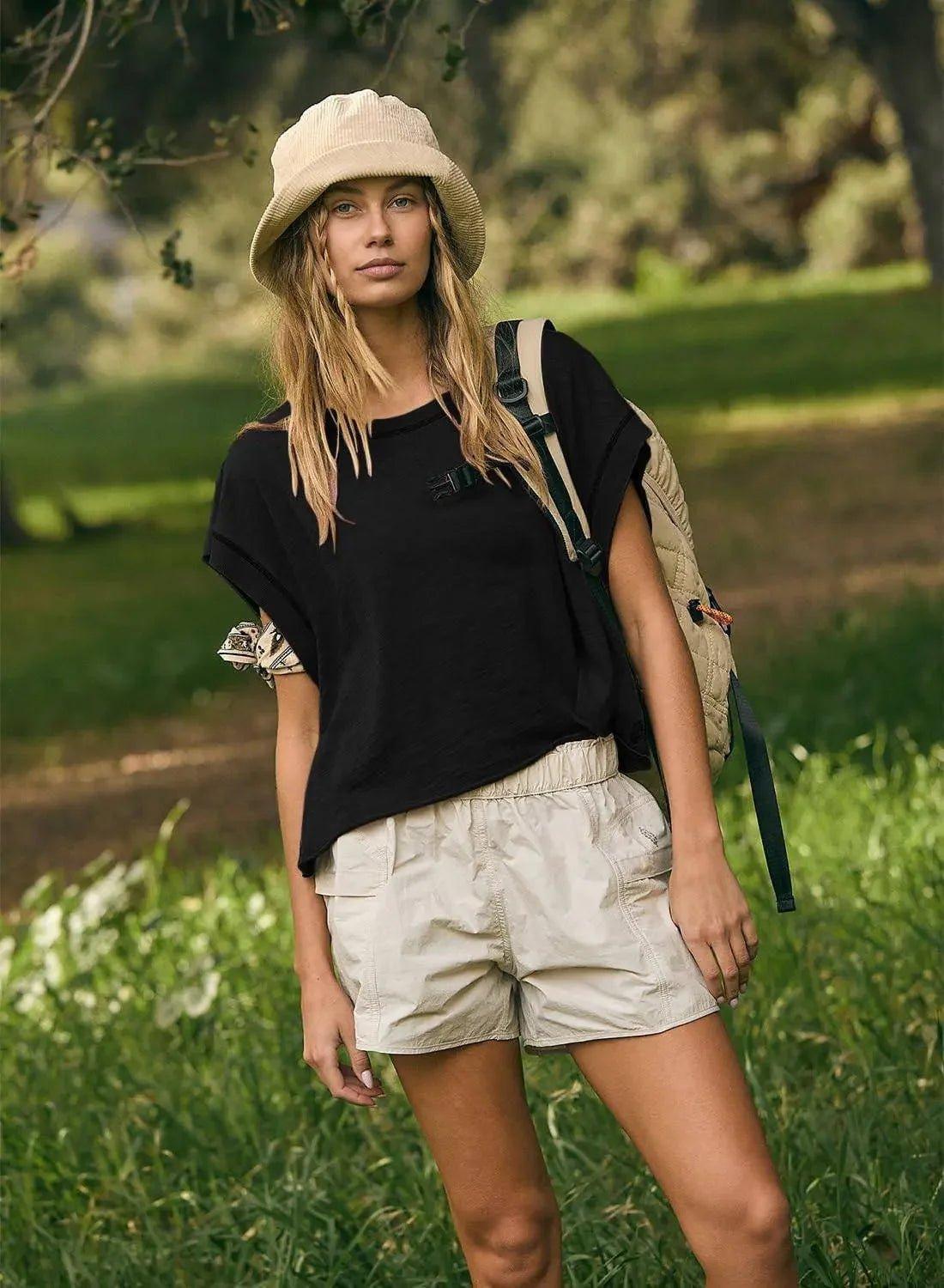 Woman in black tee, beige shorts, and corduroy bucket hat outdoors