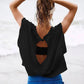 Woman in black backless top and blue pants at beach, tying wet hair