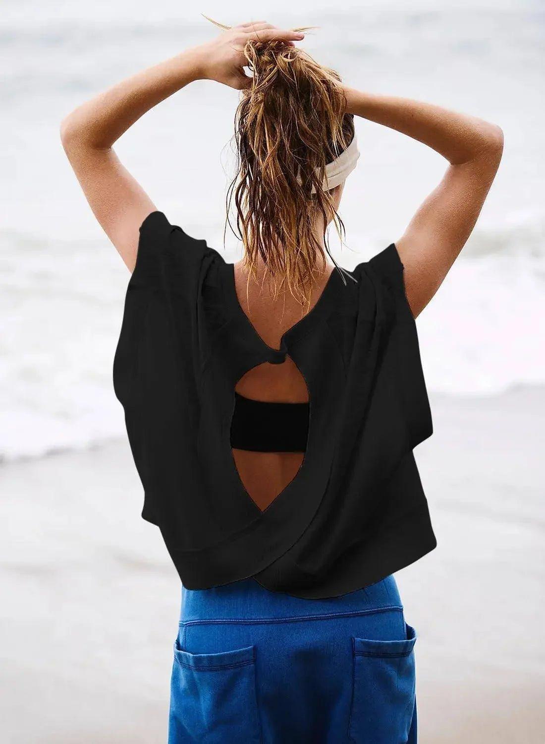 Woman in black backless top and blue pants at beach, tying wet hair