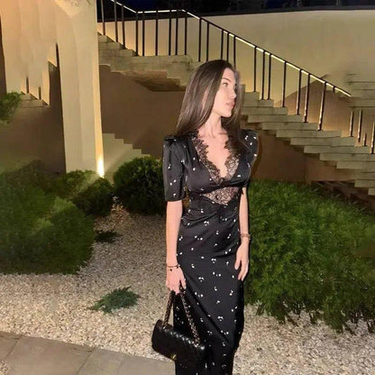 Woman in black floral dress with lace detail, holding handbag, outdoor evening setting