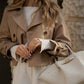 Woman in beige trench coat with white ribbed top and handbag, stylish fashion outfit
