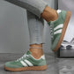 Green women's fashion sneakers with white stripes and gum sole, paired with ripped jeans