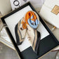 Elegant women's silk scarf with horse print, orange and blue accents, styled in luxury gift box for fashion accessories.