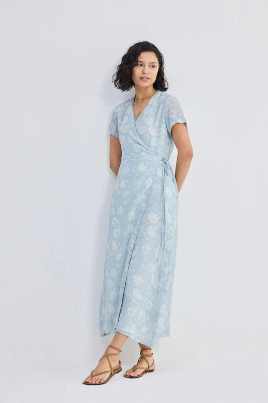 Woman in light blue floral wrap dress with short sleeves and tie waist, paired with strappy sandals