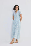 Woman in light blue floral wrap dress with short sleeves and tie waist, paired with strappy sandals