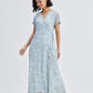 Woman in light blue floral wrap dress with short sleeves and tie waist, paired with strappy sandals