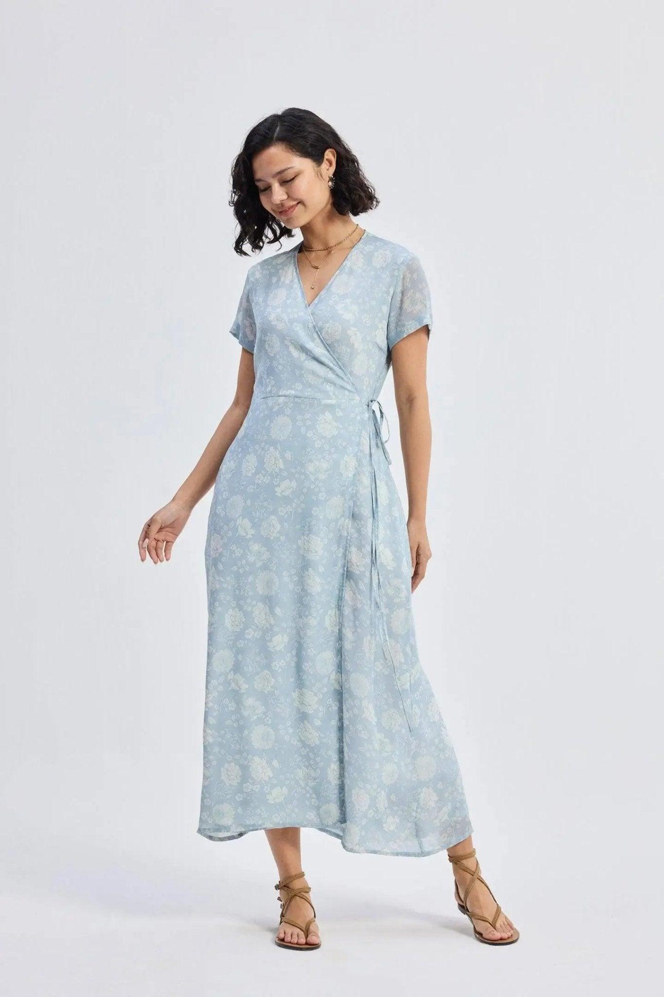 Woman in light blue floral wrap dress with short sleeves and tie waist, paired with strappy sandals