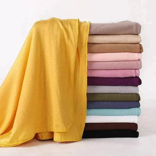 Soft yellow scarf draped over stack of colorful fashion scarves for women