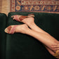 Women's embroidered flat sandals with brown straps, styled on a green velvet couch
