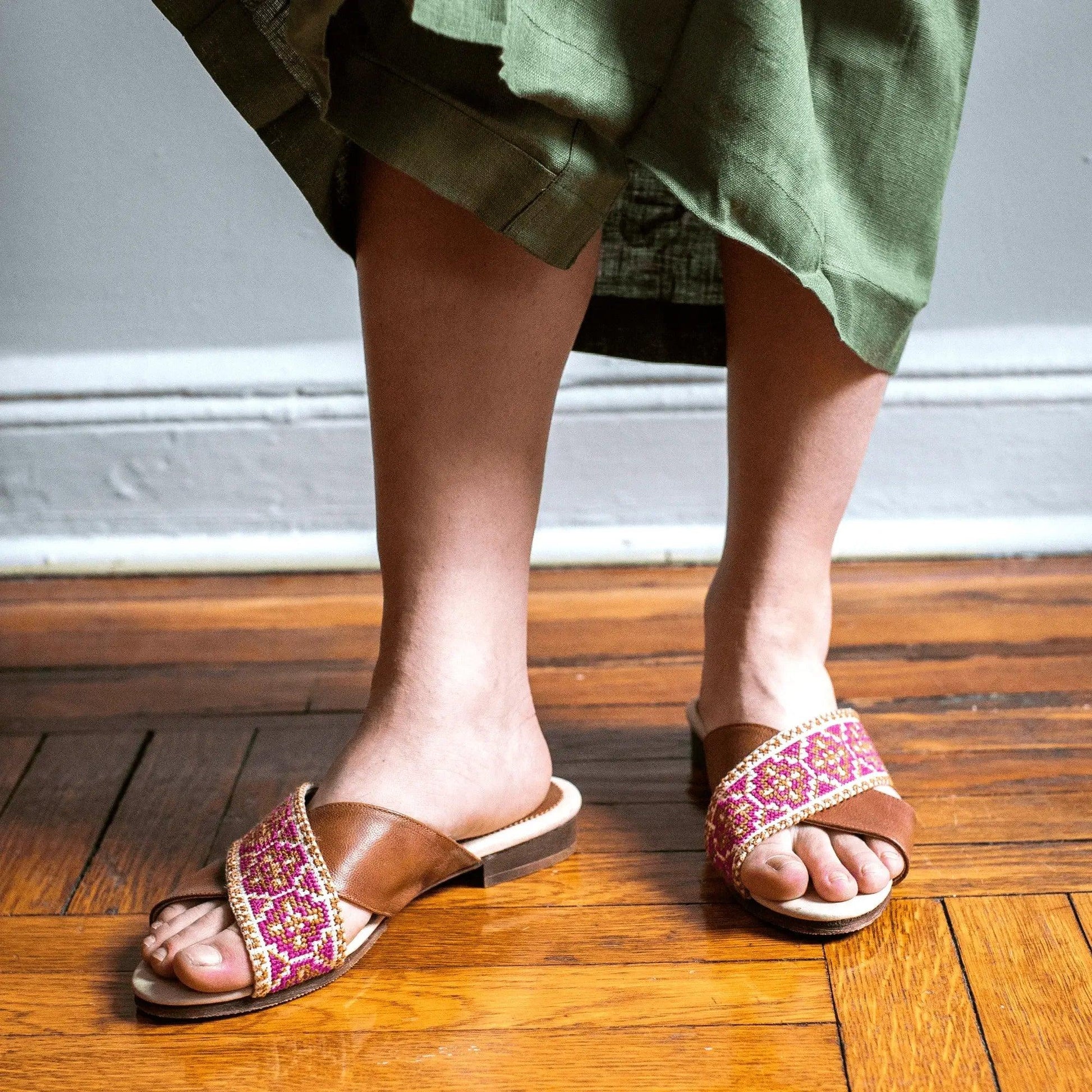 Women's embroidered slide sandals with pink pattern, paired with green dress on wooden floor