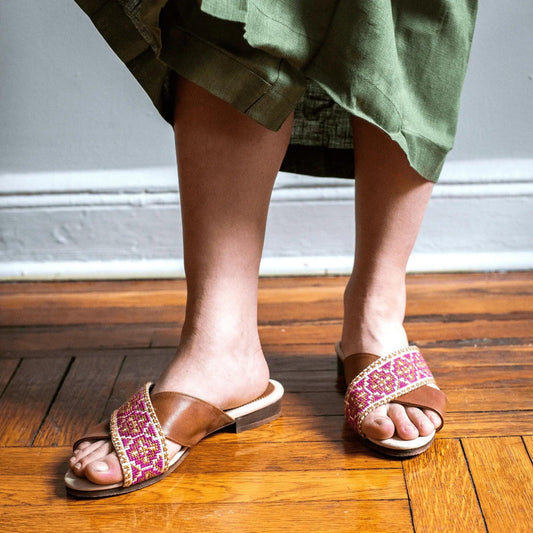Women's embroidered slide sandals with pink pattern, paired with green dress on wooden floor